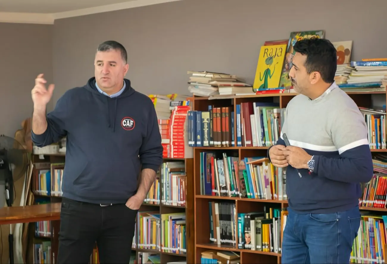 Dos expositores conversan frente a una biblioteca durante la capacitación.